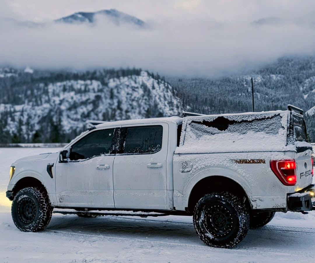 A WildTop soft truck cap dusted in snow on a Ford F-150, snow-covered mountains behind it